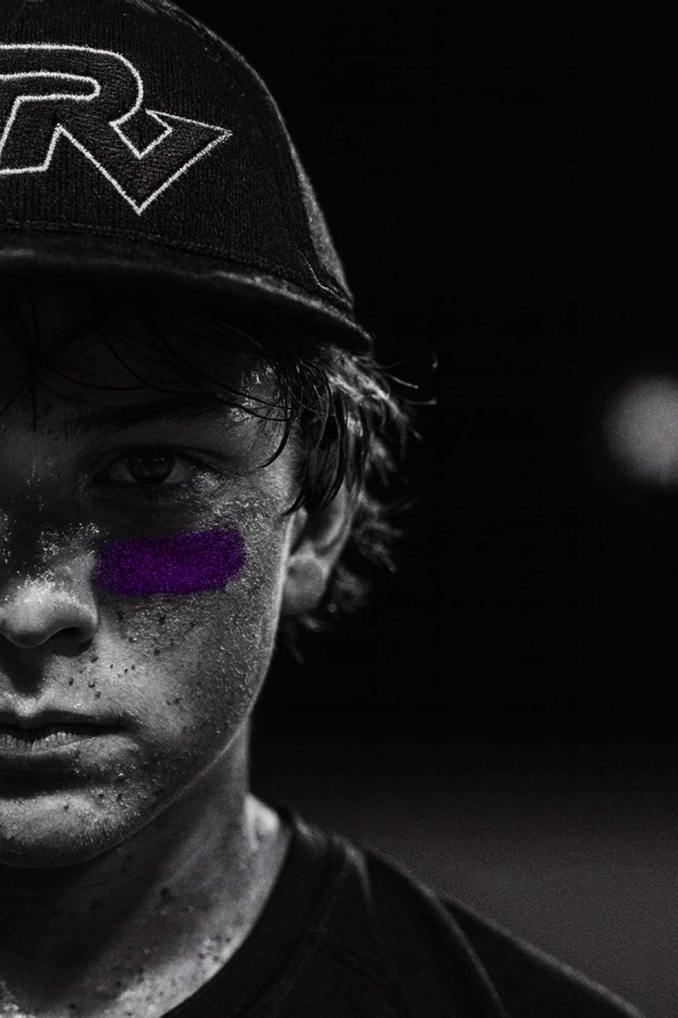 Half of a Ravens baseball player's face at the edge of the frame, purple eye black under his eye