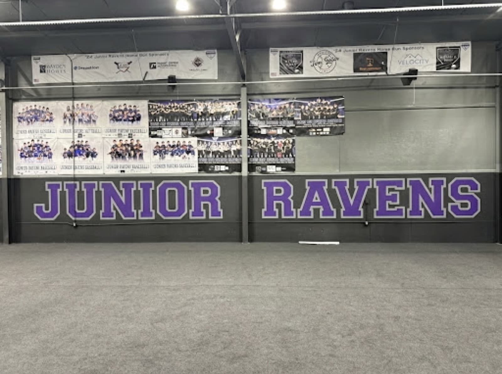 The JUNIOR RAVENS lettering across the clubhouse wall, above the black turf