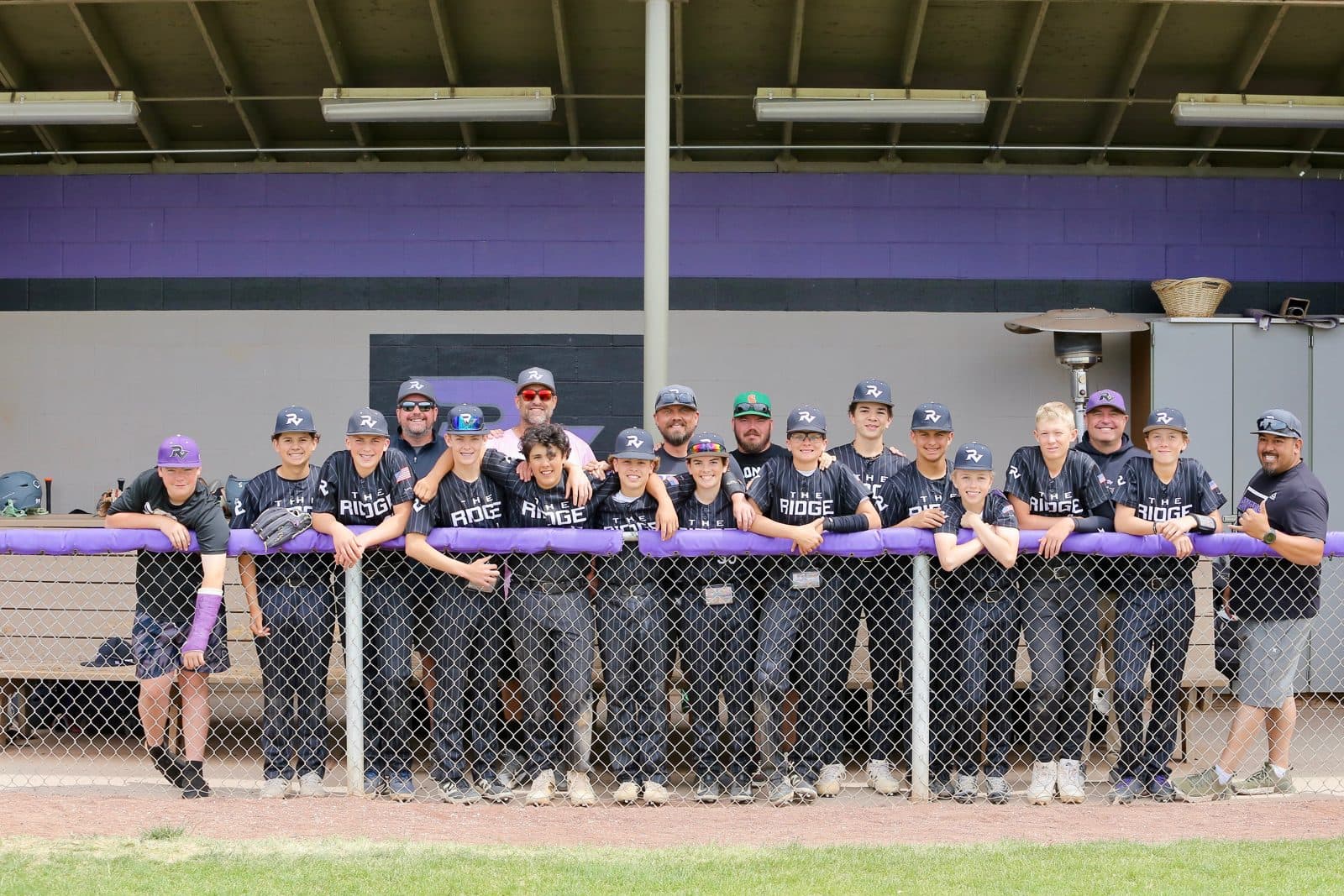 A Ravens baseball team and its coaches lined up along the purple dugout rail