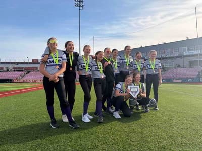 The Ravens softball team with medals and the home-plate trophy on a stadium field