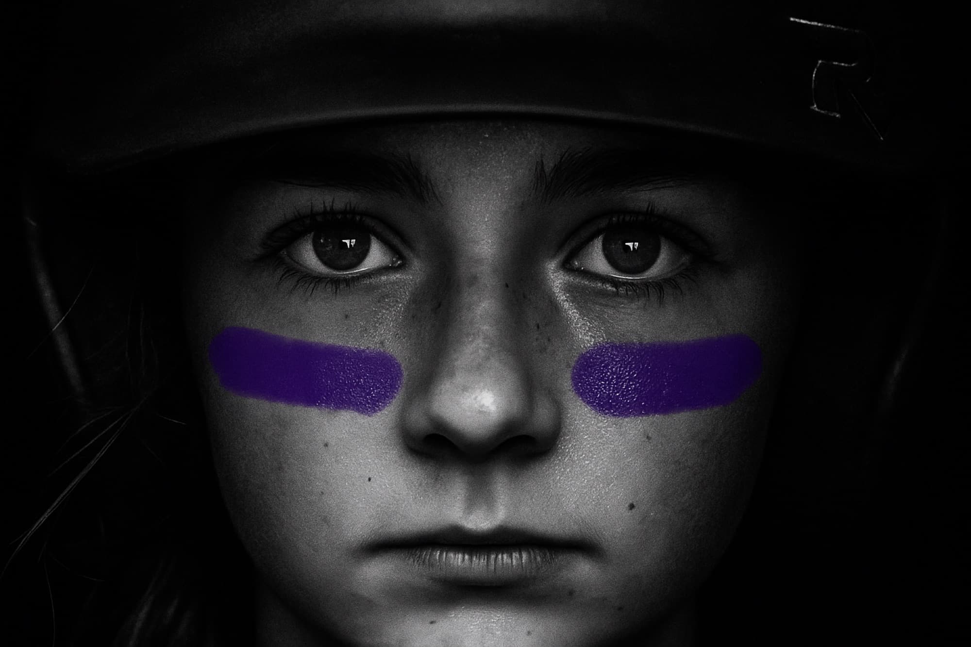 A Ravens softball player's face under her batting helmet, purple eye black striped beneath her eyes